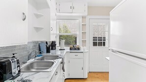 A compact kitchen with white cabinetry, a marble countertop, a coffee bar, and a dishwasher. - Midway Marvel: Central Location, Walk to Light Rail, Fast WiFi, Free Parking (Saint Paul)