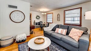 A living room with a gray sofa, a round coffee table, and a patterned rug. There are ottomans, a decorative wall piece, and a wreath on the wall. - Ancient City Cottage (St. Augustine)