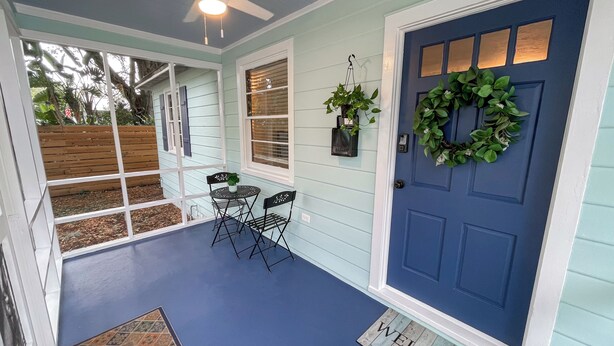 A porch with a blue door, a welcome mat, a ceiling fan, and a small table with chairs. - Ancient City Cottage (St. Augustine)