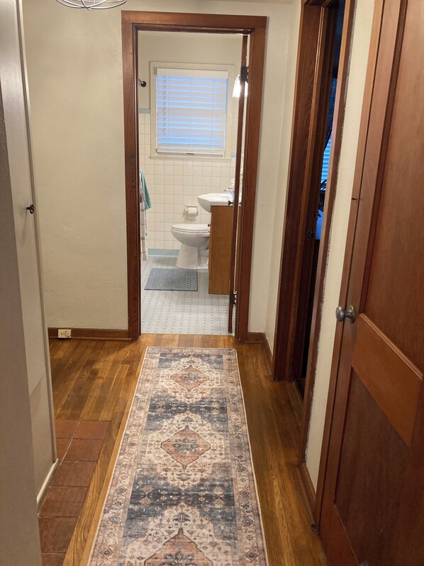 A hallway leading to a bathroom with a toilet, sink, and window with blinds. - Ancient City Cottage (St. Augustine)