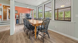 A dining area with a wooden table and chairs, a kitchen in the background, and large windows with a view of trees. - Spacious 3-bedroom home with WiFi, smart TVs, in the peaceful 4x4 area of Corova (Corolla)