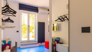 Ett modernt hotellrum med ett blått golv, en stor spegel, en garderob och ett fönster med utsikt över grönområden.