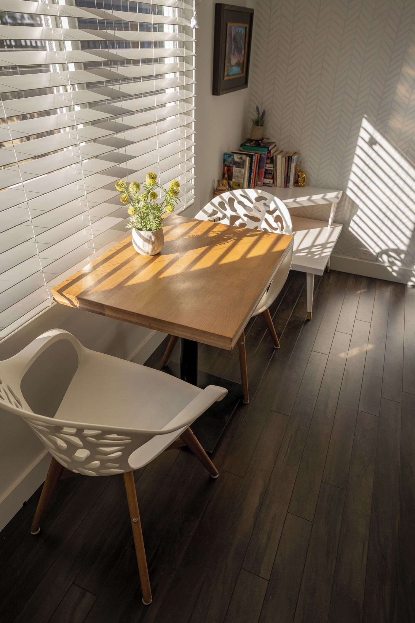 Un coin repas avec une table en bois et des chaises blanches, une plante en pot et des livres sur une étagère.