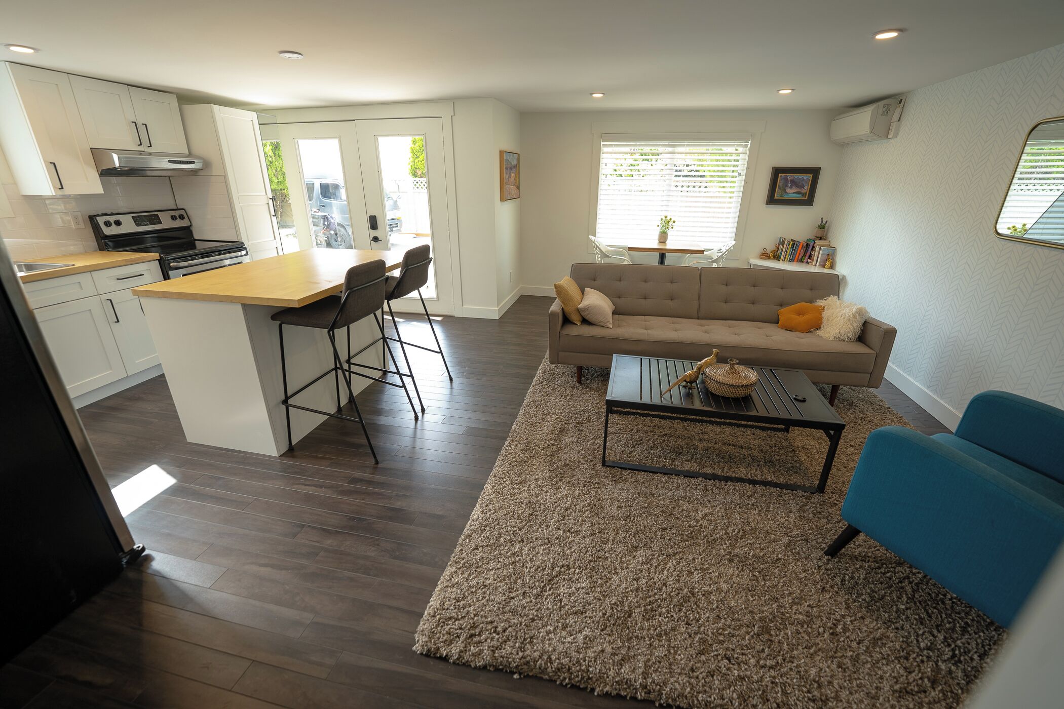 Une cuisine moderne avec des meubles blancs, un îlot central doté de tabourets de bar, un canapé beige, un fauteuil bleu et une table basse.