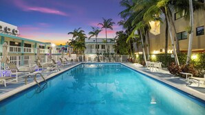 Una piscina con sillas de descanso y sombrillas, rodeada de palmeras y edificios.