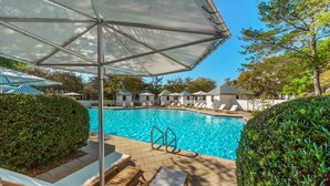 Una piscina con sillas de descanso y sombrillas, rodeada de setos y árboles bien cuidados.