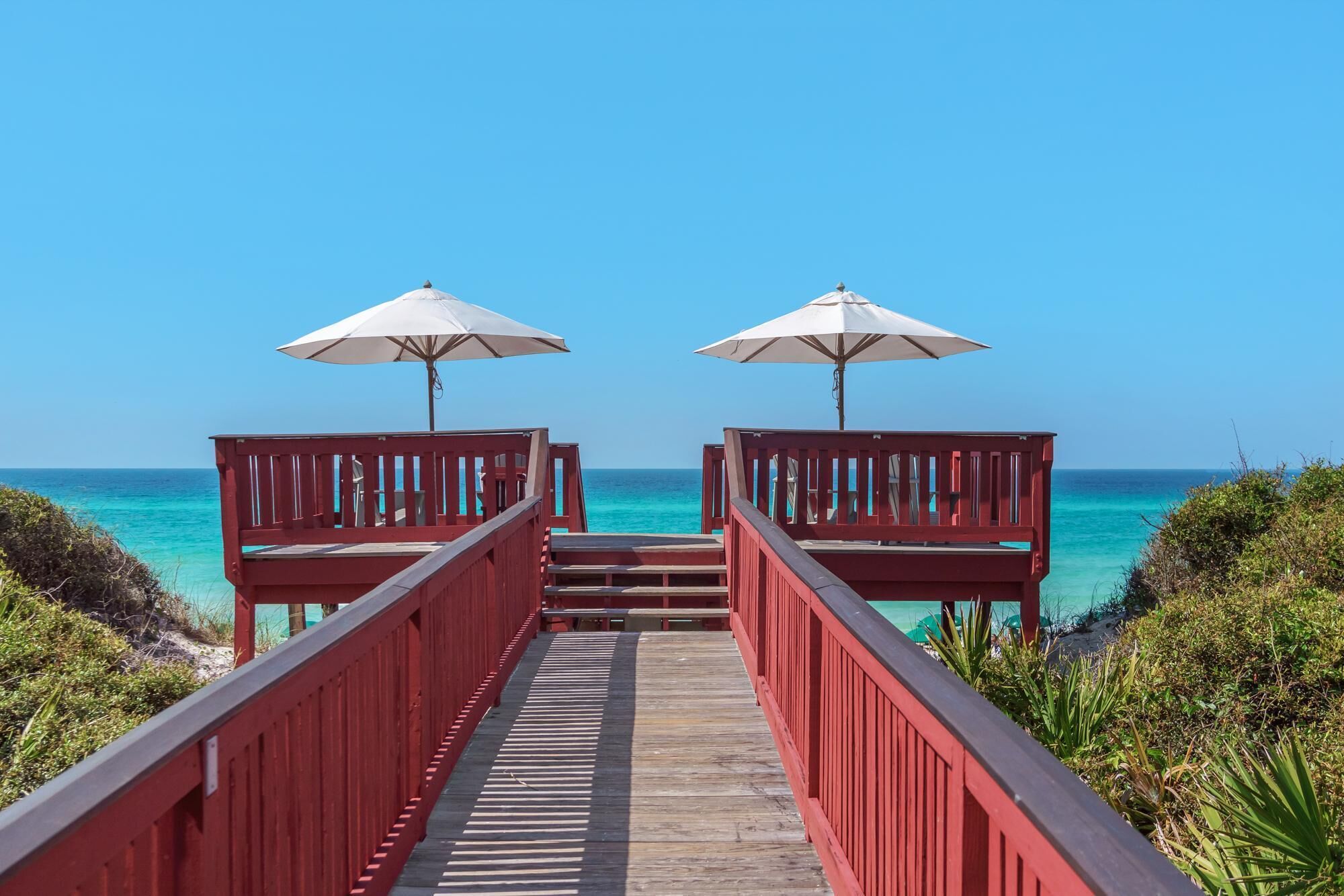 Pasarela de madera que lleva a sombrillas de playa, con vistas al océano azul turquesa.