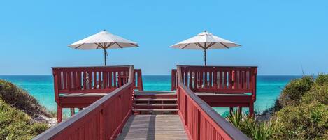 Pasarela de madera que lleva a sombrillas de playa, con vistas al océano azul turquesa.