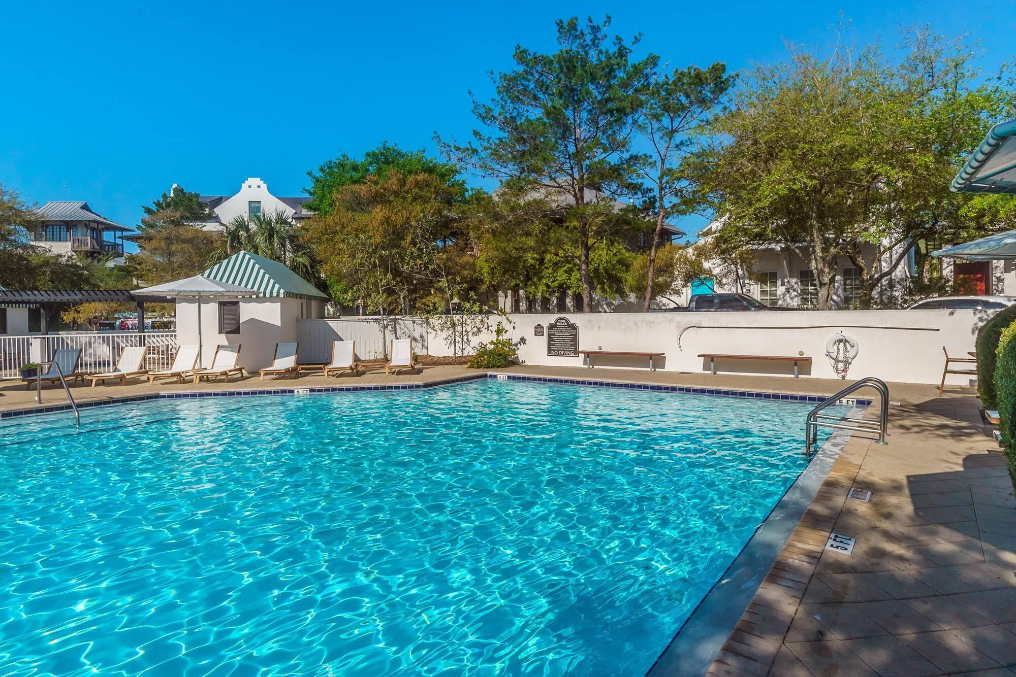 A clear blue swimming pool with lounge chairs and a small pavilion.