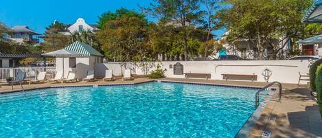 A clear blue swimming pool with lounge chairs and a small pavilion.