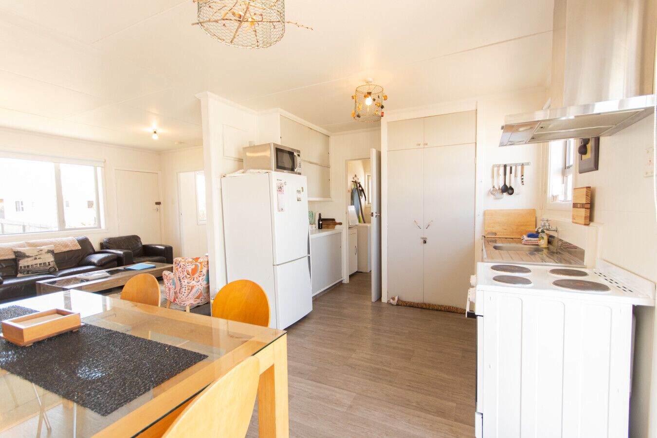A modern kitchen with a refrigerator, microwave, and stove, a dining area with a glass table and chairs, and a living room with a sofa and a coffee table.