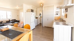 A modern kitchen with a refrigerator, microwave, and stove, a dining area with a glass table and chairs, and a living room with a sofa and a coffee table. - Aoraki Oasisl, FREE WIFI & SKY TV (Twizel)