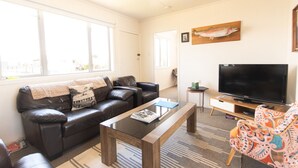 A living room with a leather sofa, a coffee table, a TV, and a large window. - Aoraki Oasisl, FREE WIFI & SKY TV (Twizel)