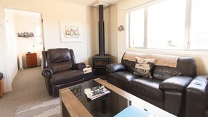 A living room with a fireplace, leather sofas, a coffee table, and a bookshelf. - Aoraki Oasisl, FREE WIFI & SKY TV (Twizel)