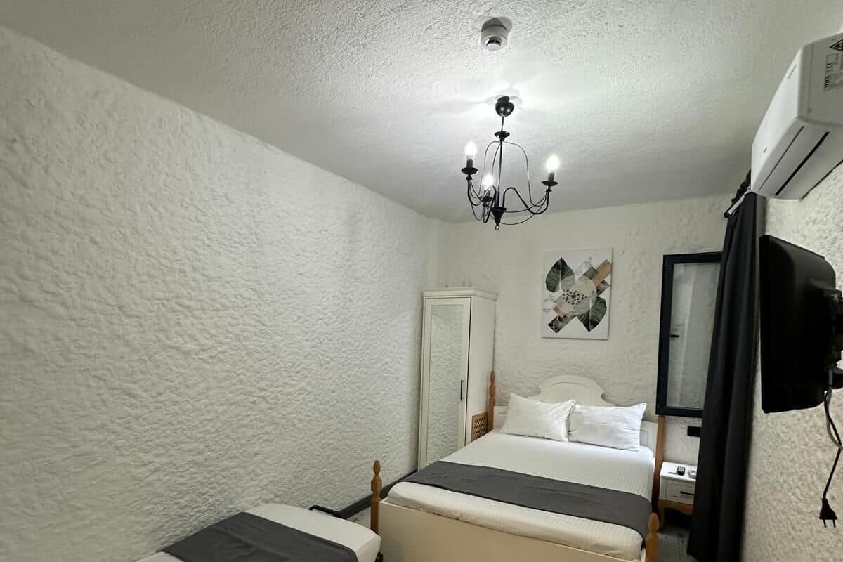 A small, compact room with two single beds, a ceiling light, a wardrobe, and a television.