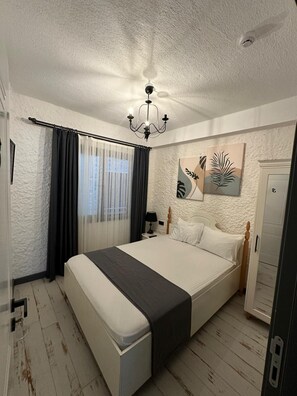 A bedroom with a bed, a chandelier, a nightstand, a lamp, and artwork on the wall. - Novas Hotel Alaçatı (Cesme)