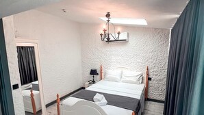 A hotel room with a bed, a nightstand, a lamp, a chandelier, and a window with curtains. - Novas Hotel Alaçatı (Cesme)