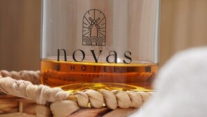 A glass of amber liquid with "novas HOTEL" and "ALACATI" embossed on it, placed on a woven mat. - Novas Hotel Alaçatı (Cesme)