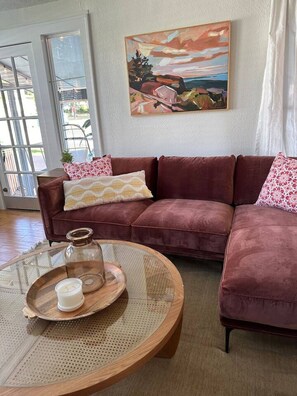 A living room with a sofa, a glass coffee table with a candle, and a painting on the wall. - Casita Encanta-Dora, Steps to town, Pet-Friendly (Mount Dora)