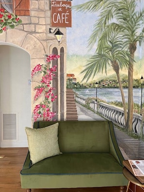 A green sofa with a cushion, a wall mural of a coastal scene, a cafe sign, and a lamp. - Casita Encanta-Dora, Steps to town, Pet-Friendly (Mount Dora)