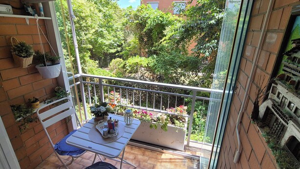 Un balcón con una mesa, sillas y plantas colgantes.