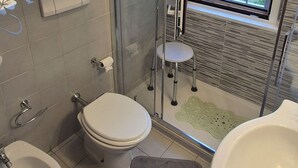 Un baño con inodoro, bidé y lavamanos. Cuenta con un box de ducha de vidrio y una ventana con vistas al exterior.