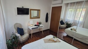 Habitación de hotel con cama, escritorio con lámpara, silla, televisor, espejo y ventana con cortinas.