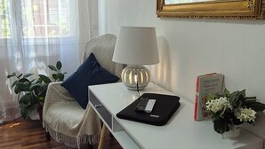 Una sala de estar moderna con un escritorio blanco, una lámpara, un espejo y un televisor. Hay plantas y un libro sobre el escritorio.