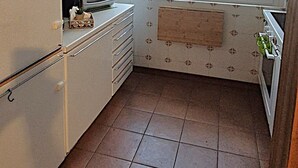 Cocina compacta con refrigerador, microondas y estufa. Hay una ventana con persianas y un ventilador de techo.