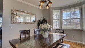 A dining room with a large wooden table, two chairs, a white vase with flowers, a decorative mirror, and a window with blinds. - Private Farmhouse Retreat in Shoal Creek (Exeter)