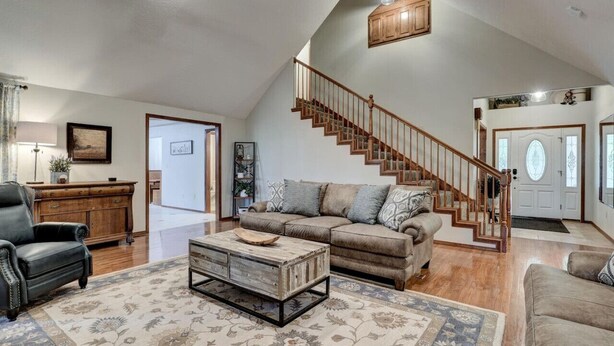 Un salon spacieux avec un plafond haut, un escalier en bois et une grande fenêtre.