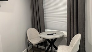 A small room with a round table and two chairs, a TV mounted on the wall, and a window with curtains.
