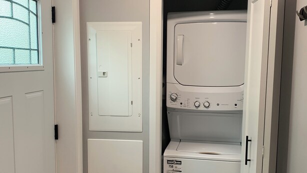 A laundry room with a front-loading washer and dryer, a door with a window, and a wall-mounted vent.