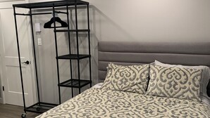 A bedroom with a patterned bedspread, a grey headboard, and a black metal wardrobe with a hanging rack.