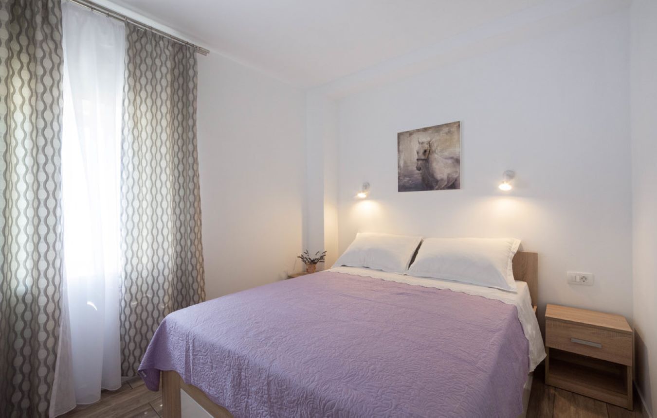 A bedroom with a bed, a nightstand, a wall-mounted painting, and a window with patterned curtains.
