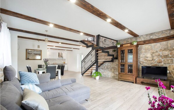 A spacious living area with a grey sofa, a wooden staircase, a stone wall, and a TV.