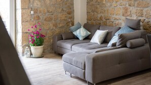Un salón con una pared de piedra, un sofá gris y una maceta con flores rosas.