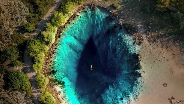 Vista aérea de una zona costera con una masa de agua azul cristalina, rodeada de vegetación y una playa de arena.