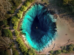 An aerial view of a coastal area with a clear blue water body surrounded by greenery and a sandy beach.