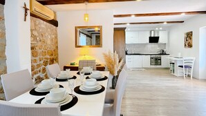 Un comedor con pared de piedra, techo de madera y vista hacia una cocina.