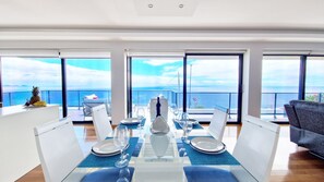 A dining area with a table set for four, large windows, and a view of the sea.