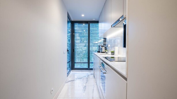 A modern kitchen with a glass door leading to a balcony, a stainless steel sink, and a white countertop.