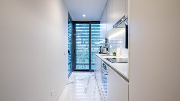 A modern kitchen with a glass door leading to a balcony, a stainless steel sink, and a white countertop.
