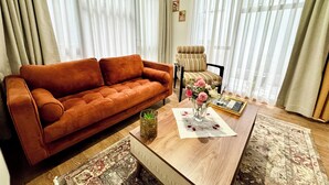 A living room with a brown sofa, a patterned armchair, a wooden coffee table with a vase of flowers, and a rug. - Modern Furnished Historical House (İstanbul)
