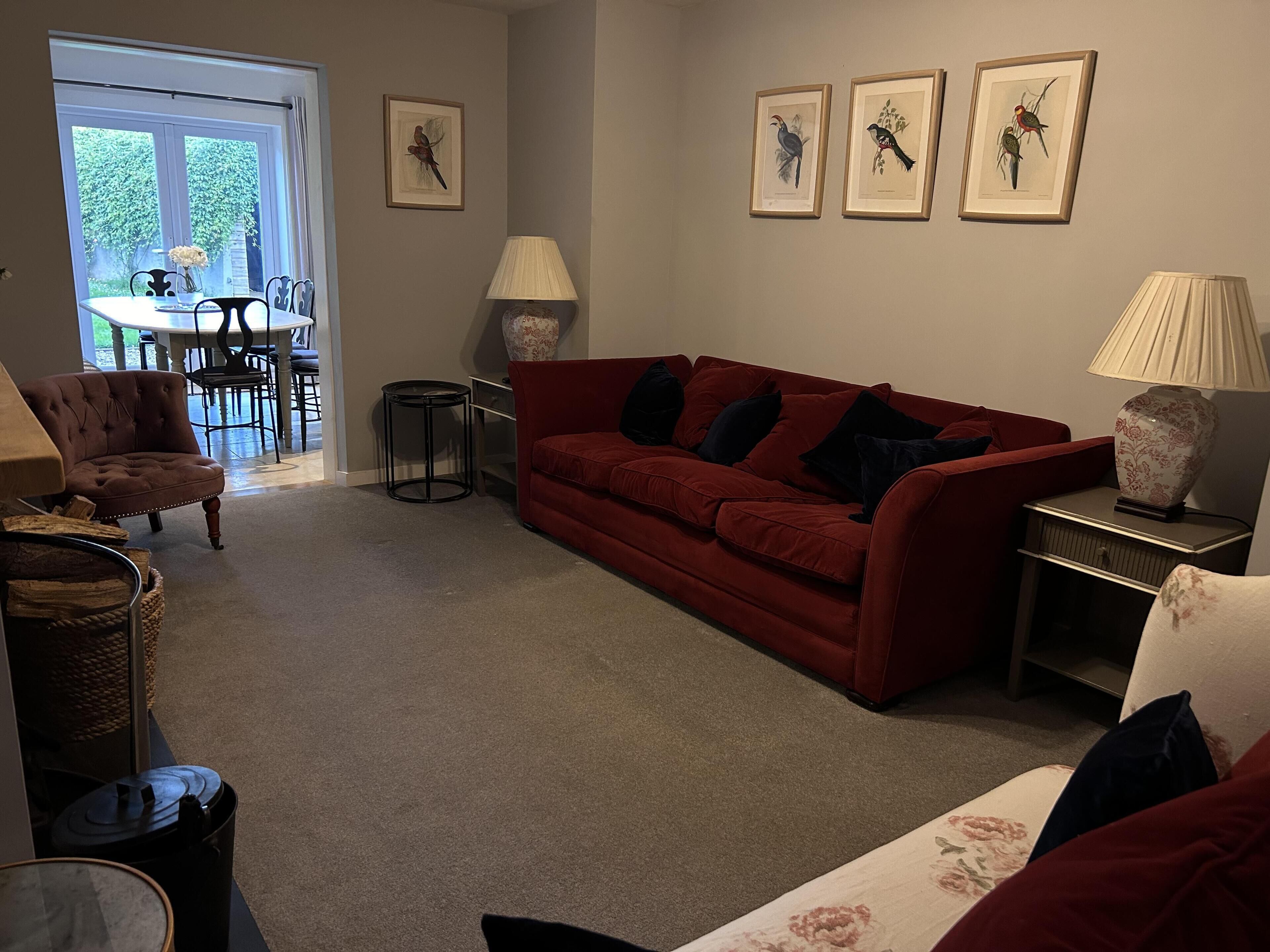 A living room with a red sofa, a small round table, a lamp, and framed bird illustrations on the wall.