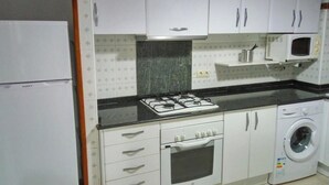 Une cuisine compacte avec des meubles blancs, une cuisinière à gaz, un four à micro-ondes et un lave-linge.