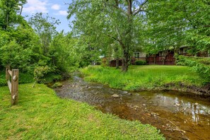 A stream flowing through a lush, green landscape with a wooden fence and a building with a deck in the background.