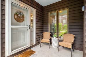 A front porch with a welcome sign, two wicker chairs, and a small table with a plant.