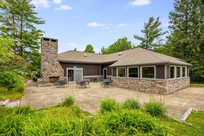 A house with a stone chimney, a covered patio with outdoor furniture, and a large windowed room. - Downtown 1st Floor | Walk to Main St + Fireplace (Blowing Rock)