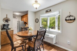 Une cuisine avec des meubles en bois, une table à manger avec des chaises, une machine à café et une fenêtre donnant sur un paysage verdoyant.